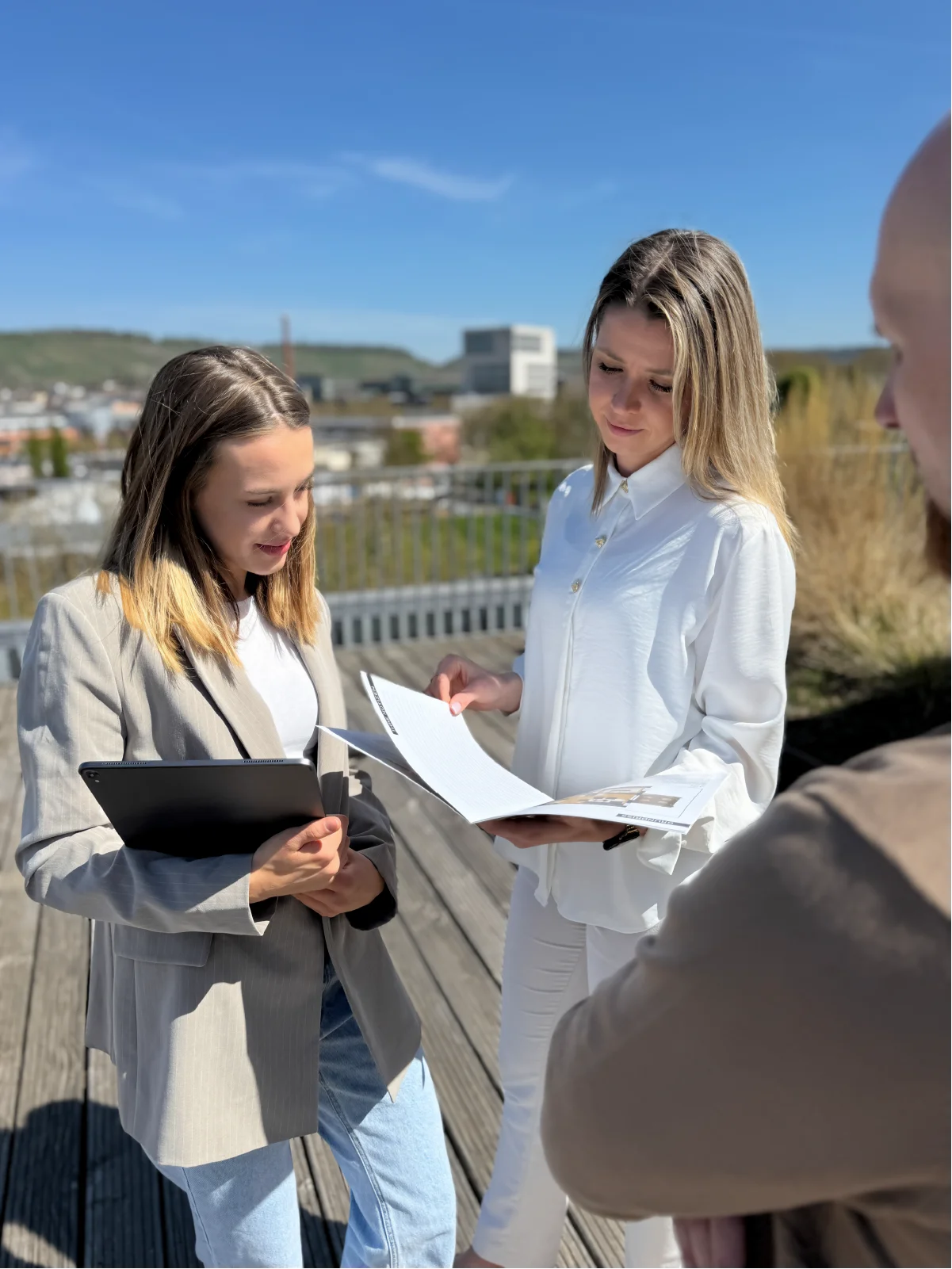 Zwei Mitarbeiterinnen von Wohlfeil besprechen ein Exposé über den Dächern von Heilbronn